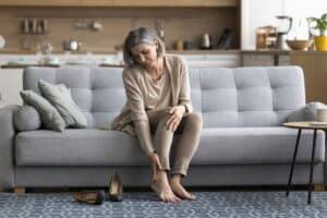 Older woman sitting inside holding her ankle in pain from venous ulcer in Minneapolis